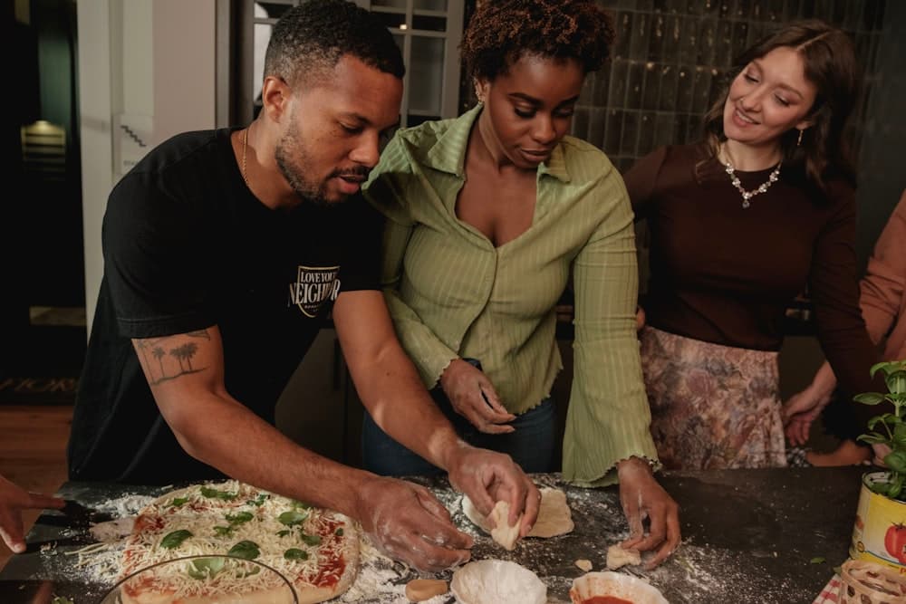 Three friends making pizza together in a kitchen